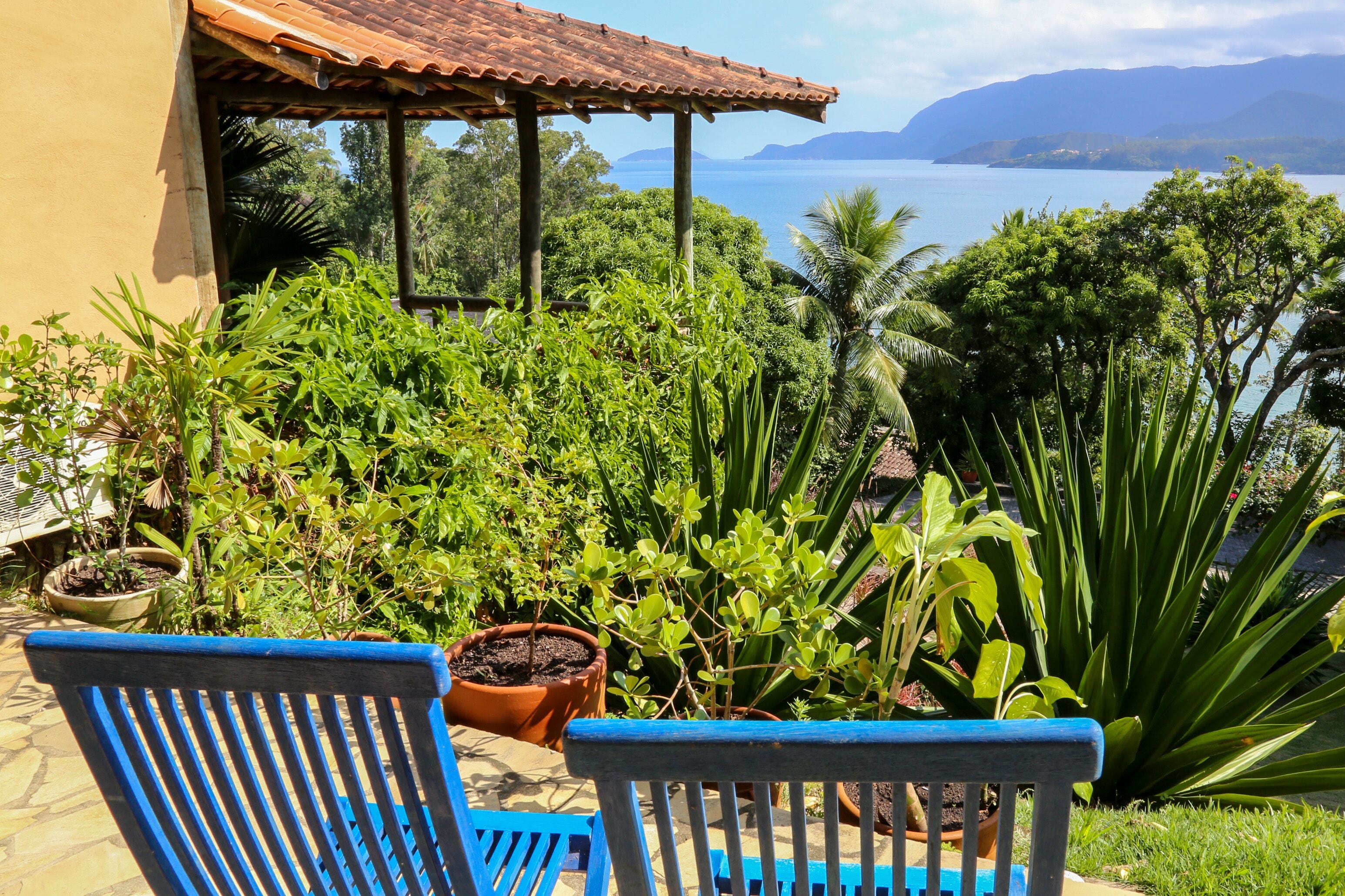 Eine Terrasse mit zwei blauen Stühlen, umgeben von Topfpflanzen und Blick auf das Meer.