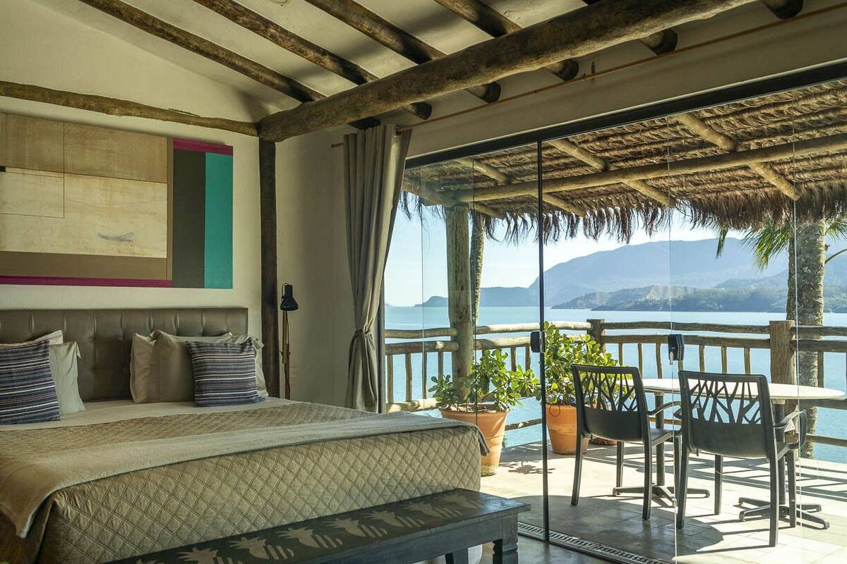 Een slaapkamer met een groot bed, een balkon met een tafel en stoelen, en uitzicht op zee.