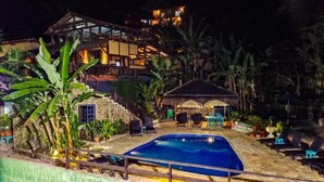 Zona de piscina con sillones de descanso, una piscina pequeña y un edificio con balcón al fondo.