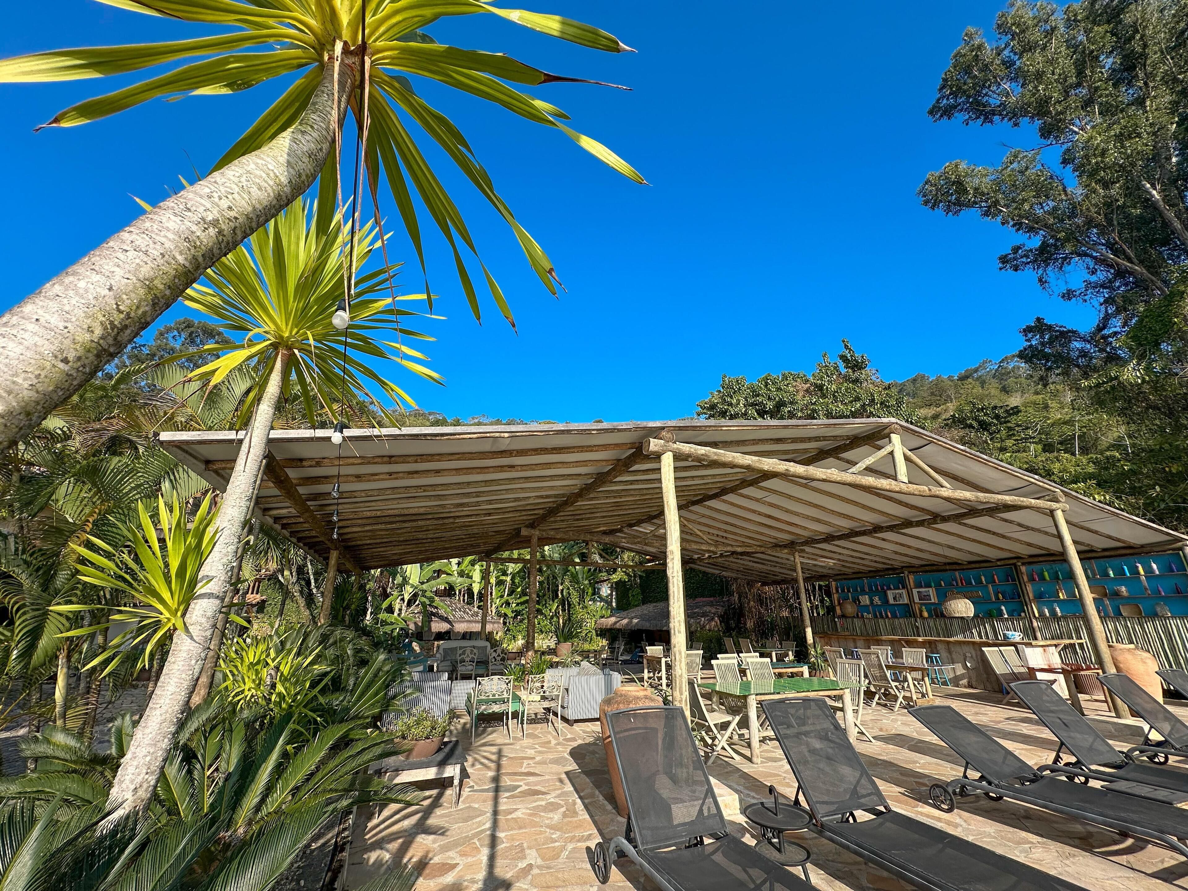 A covered outdoor seating area with lounge chairs and a thatched-roof structure in the background.