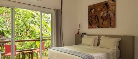 Un dormitorio con una cama grande, un ventanal corredero que da a un espacio exterior con sillas y un cuadro en la pared.