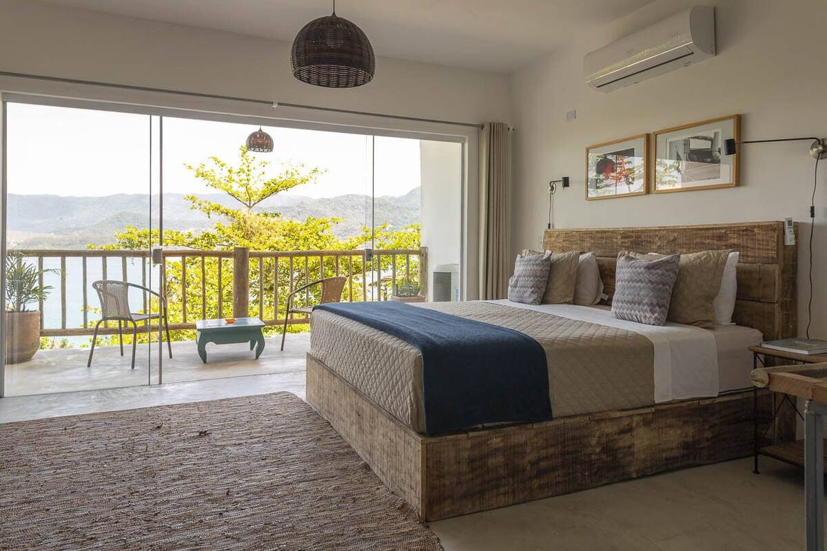 Een slaapkamer met een groot bed, uitzicht op het omliggende landschap, een balkon en een eethoek.