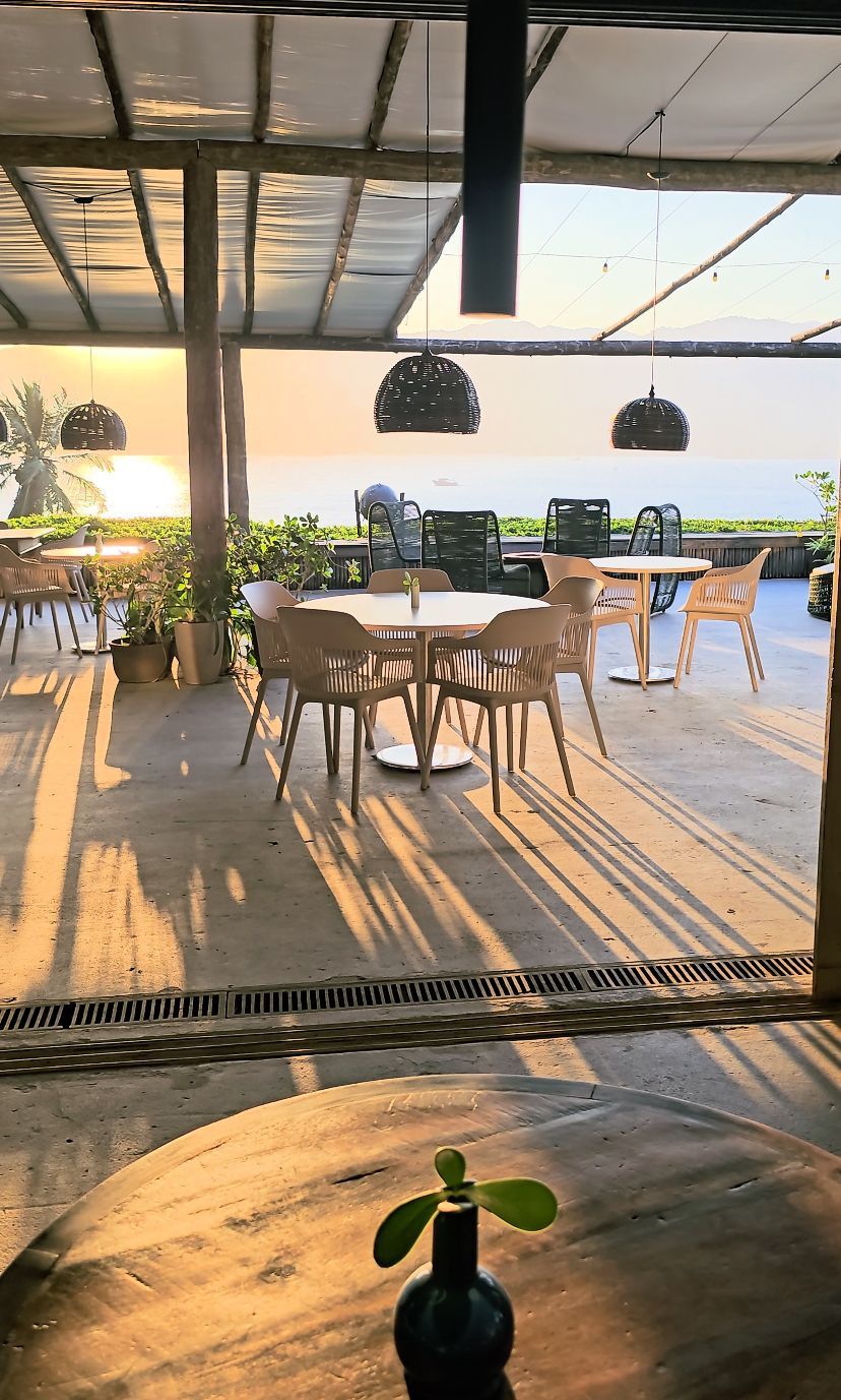 Un área de estar al aire libre con mesas y sillas, una planta en maceta y vistas al océano.