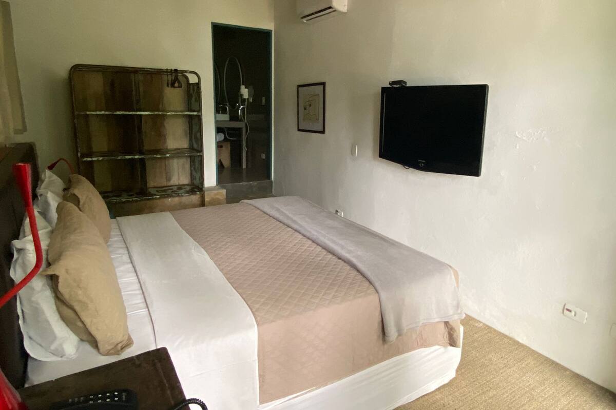 Een slaapkamer met een bed, een aan de muur bevestigde televisie en een doucheruimte zichtbaar door een geopende deur.