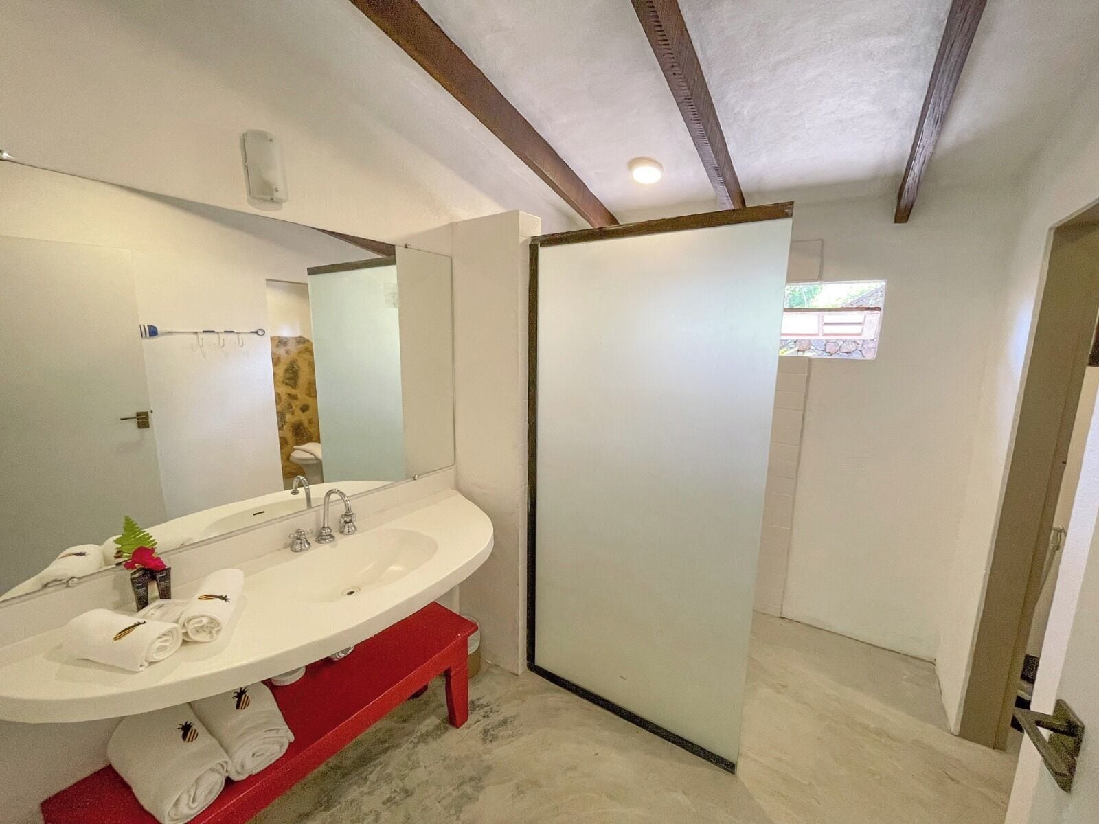 Un baño con un lavabo blanco, un espejo y un banco rojo.