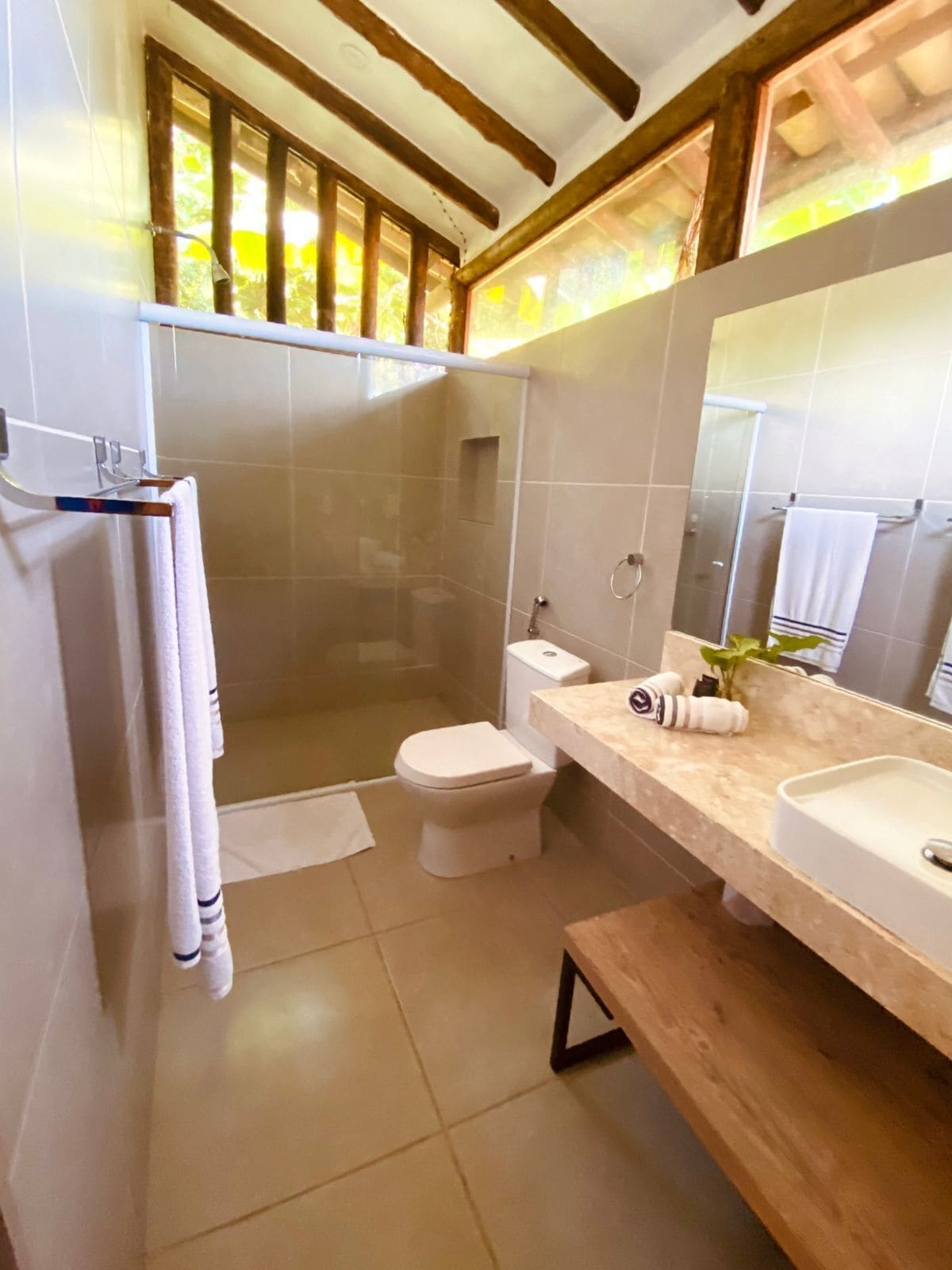 A bathroom with a shower, toilet, and sink, featuring a wooden ceiling and tiled walls.