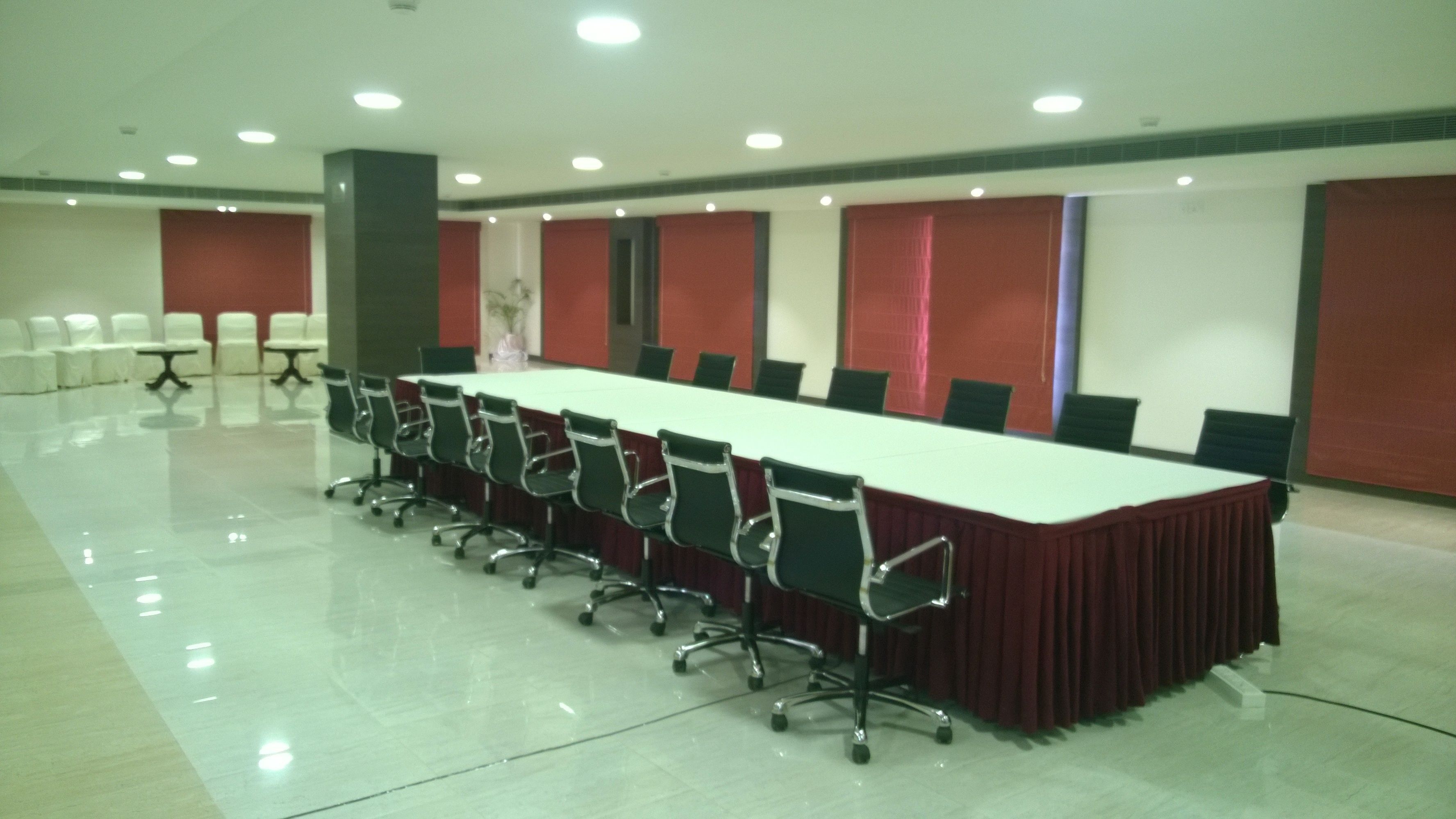 A conference room with a long table and chairs, white walls, and red accents.