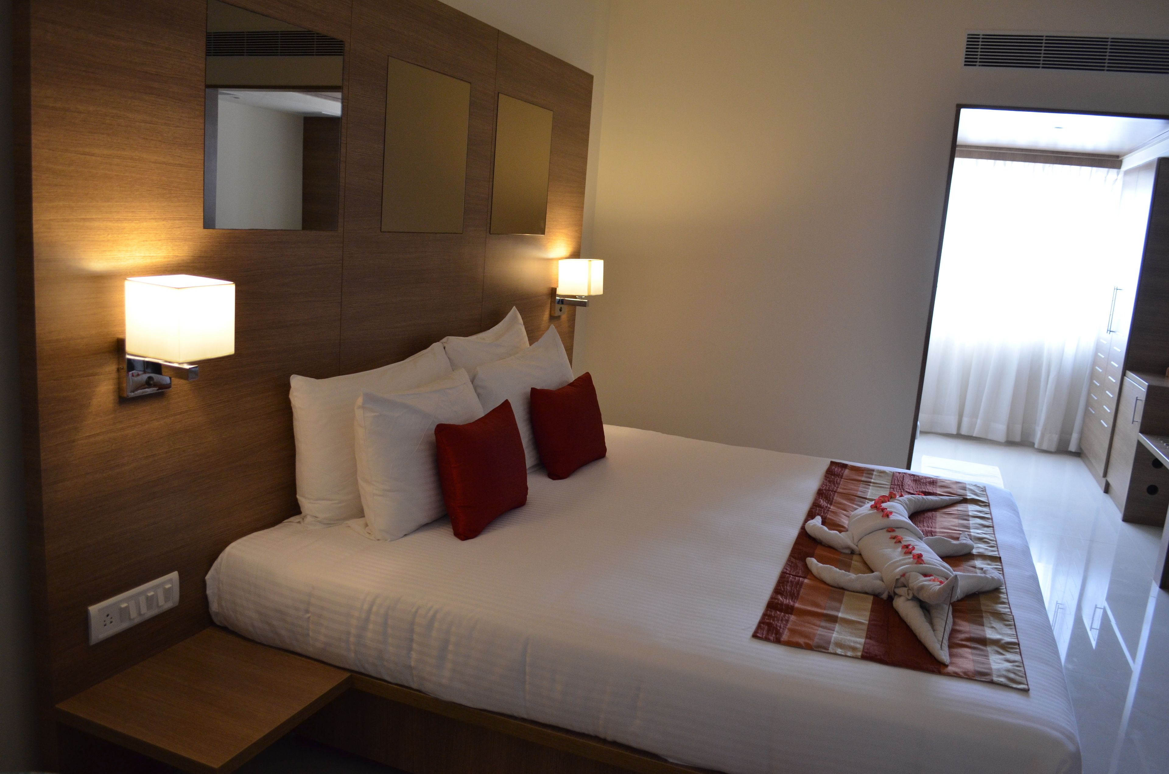A hotel room with a large bed, two bedside lamps, a wooden headboard, and a view of the outdoors.