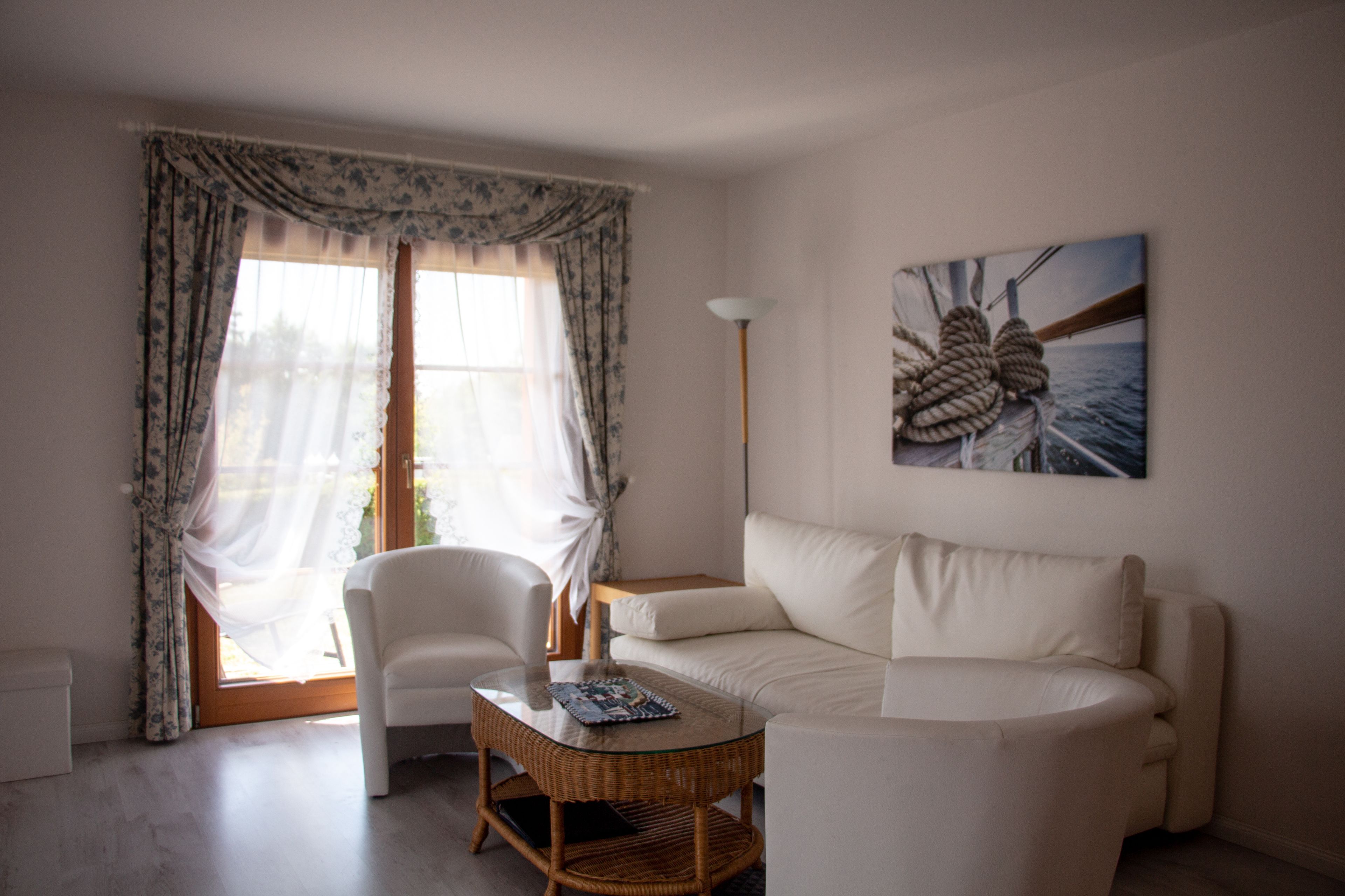 A room with a white sofa, a wicker coffee table, a chair, and a painting of a ship's anchor.