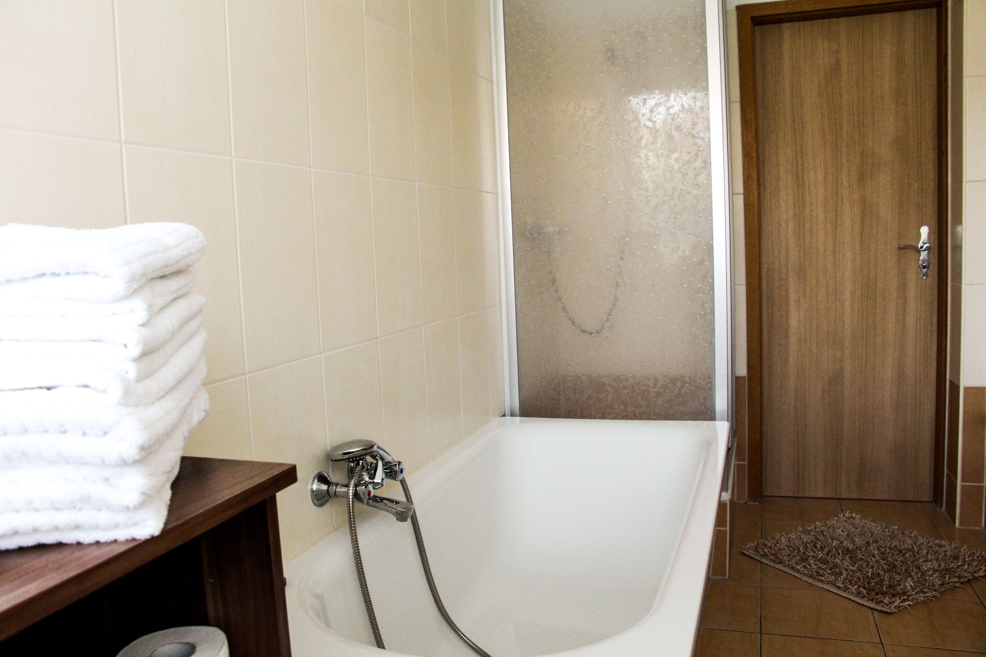 A bathroom with a bathtub, a shower, and a stack of white towels on a shelf.