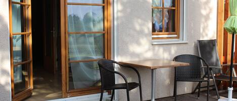 Een terras buiten met een tafel en twee stoelen, een schuifpui en een klein raam.