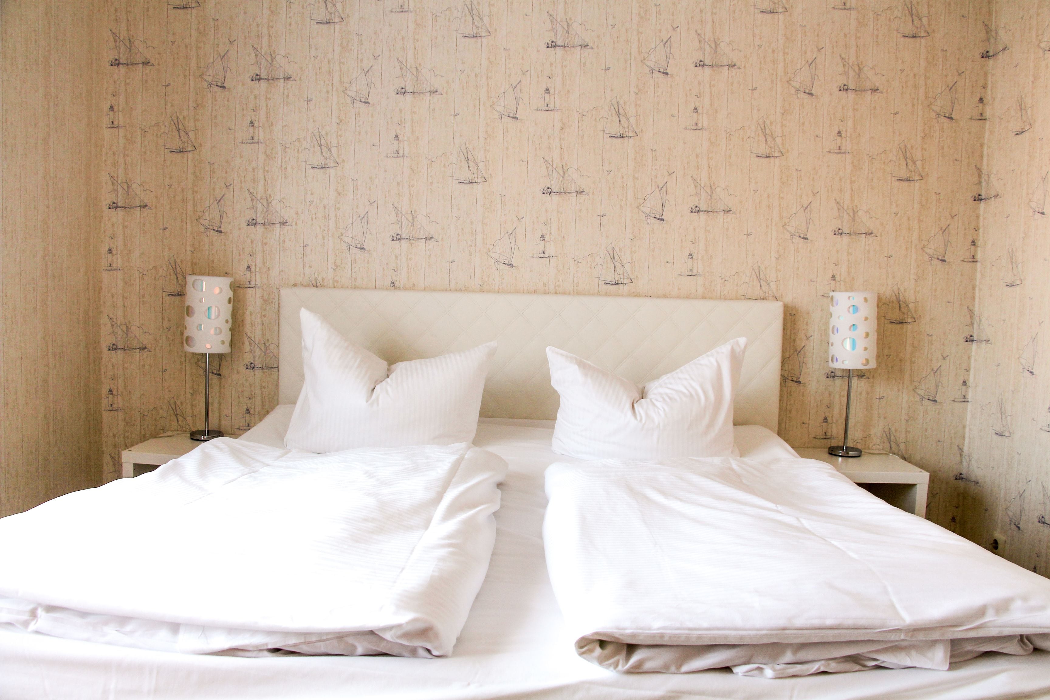 A double bed with white bedding, two bedside tables with lamps, and a wooden wall with a sailboat pattern.