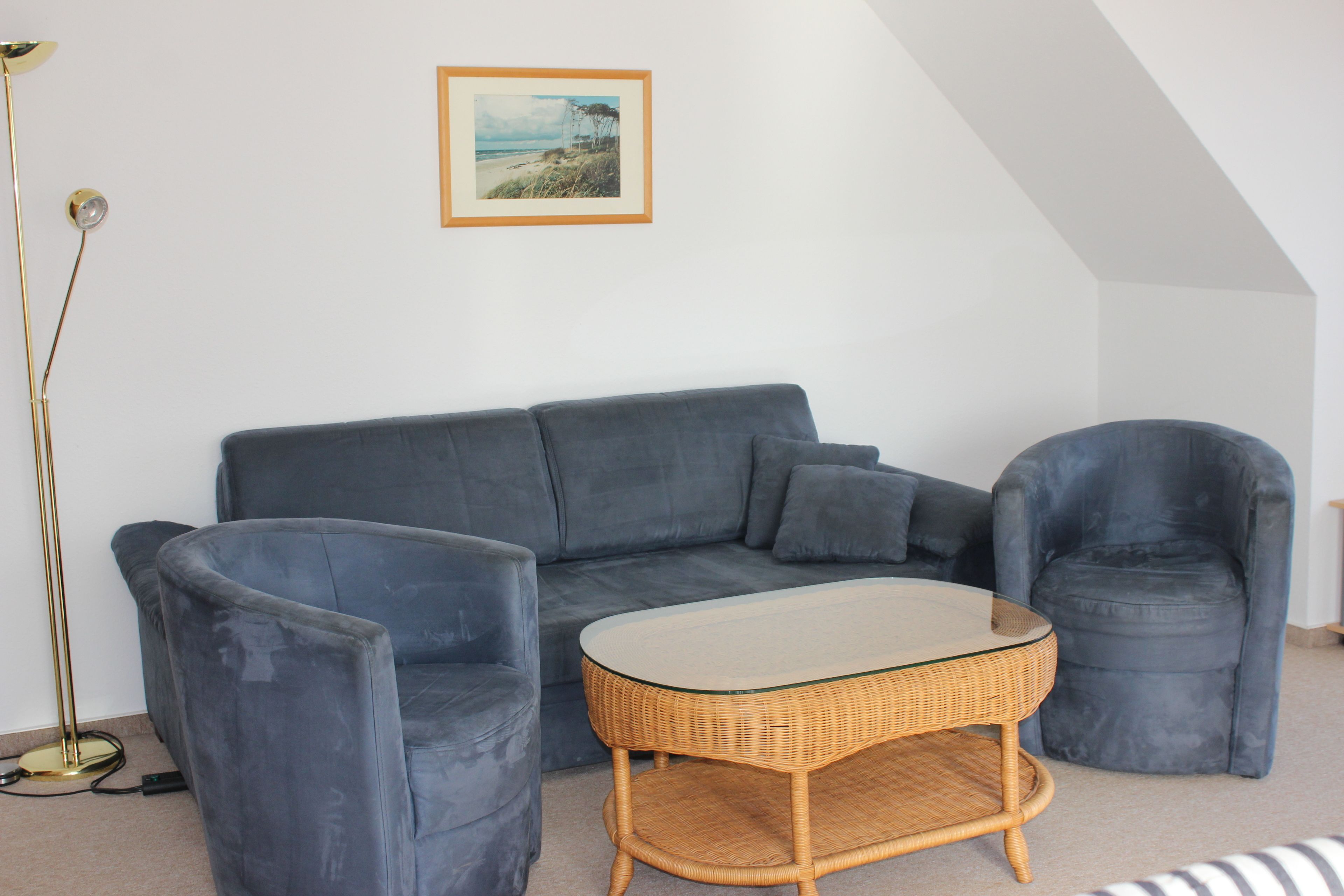 A living room with a grey sofa, two armchairs, a glass-top coffee table, and a floor lamp.