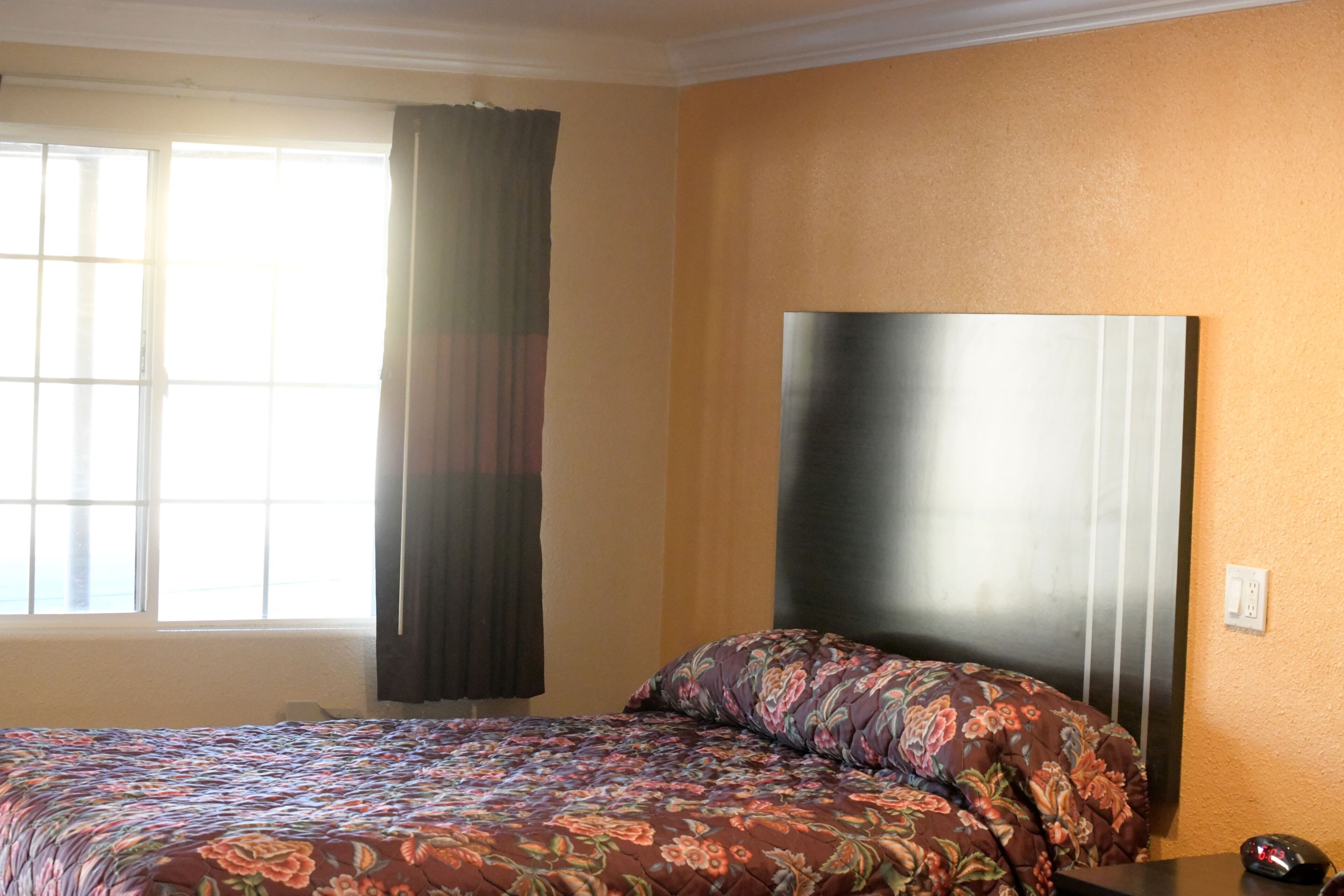 A hotel room with a bed, a large window with curtains, and a wall-mounted headboard.