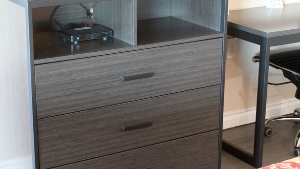 A wooden desk with a drawer unit and a black electronic device on top.