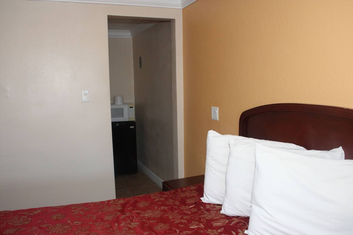 Quarto de hotel com cama, cabeceira de madeira e colcha vermelha estampada.
