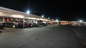 A parking lot with several cars parked in front of a building with multiple doors.