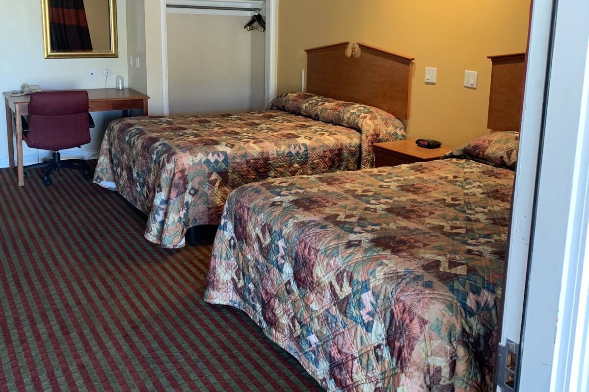 Quarto de hotel com duas camas, uma escrivaninha, uma cadeira e um espelho.