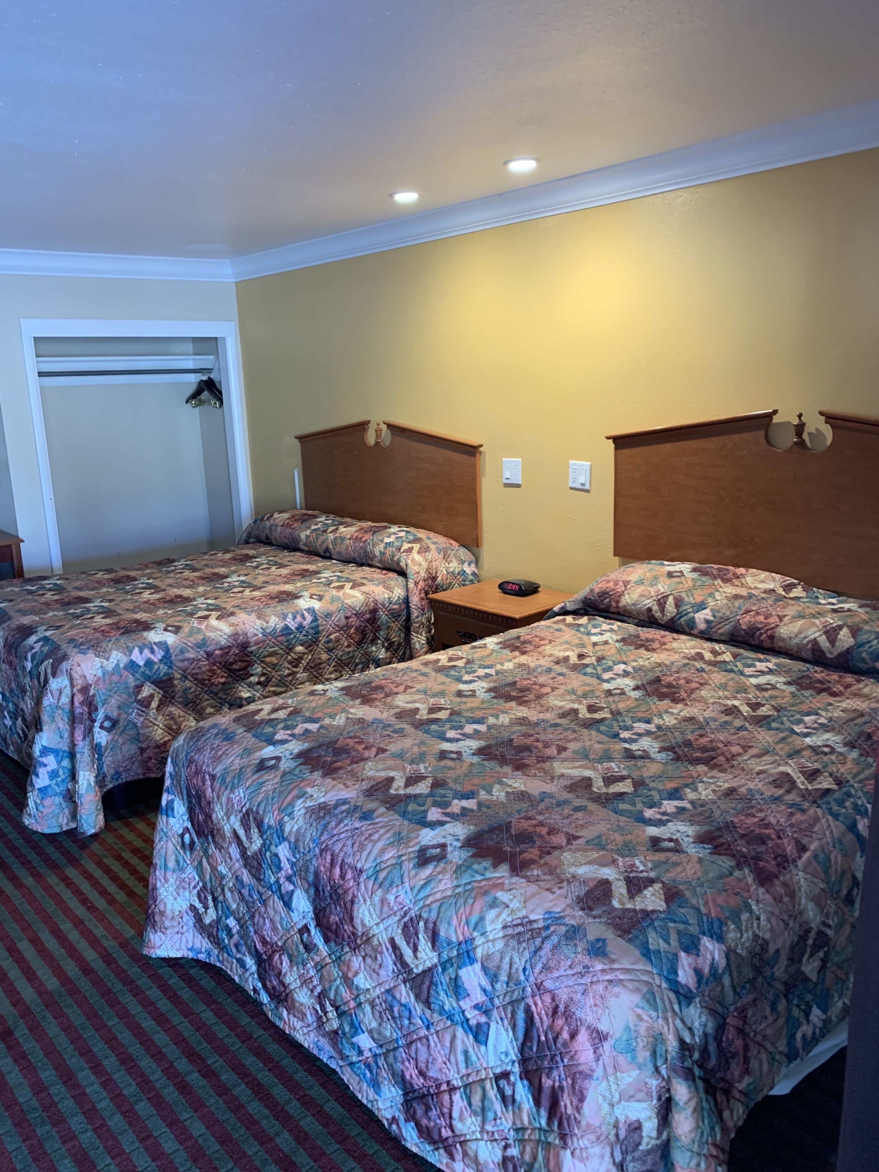 Habitación de hotel con dos camas, un cabecero de madera, una mesita de noche de madera y un armario con espejo.
