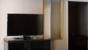 A television on a black stand with a gold-framed mirror above it, and a door leading to a dark room.