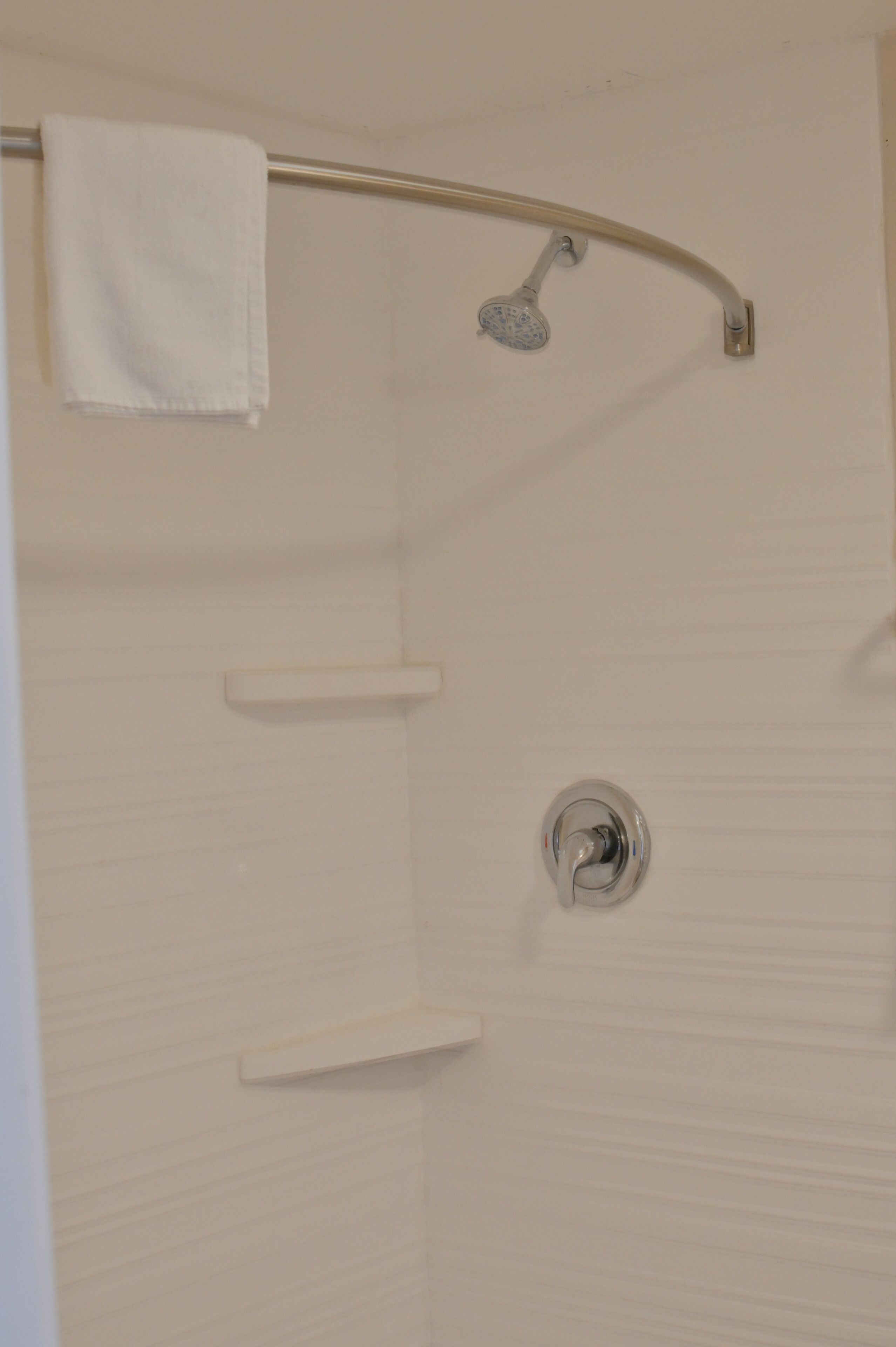 A shower area with a towel hanging on a rod, a showerhead, and a wall-mounted shelf.