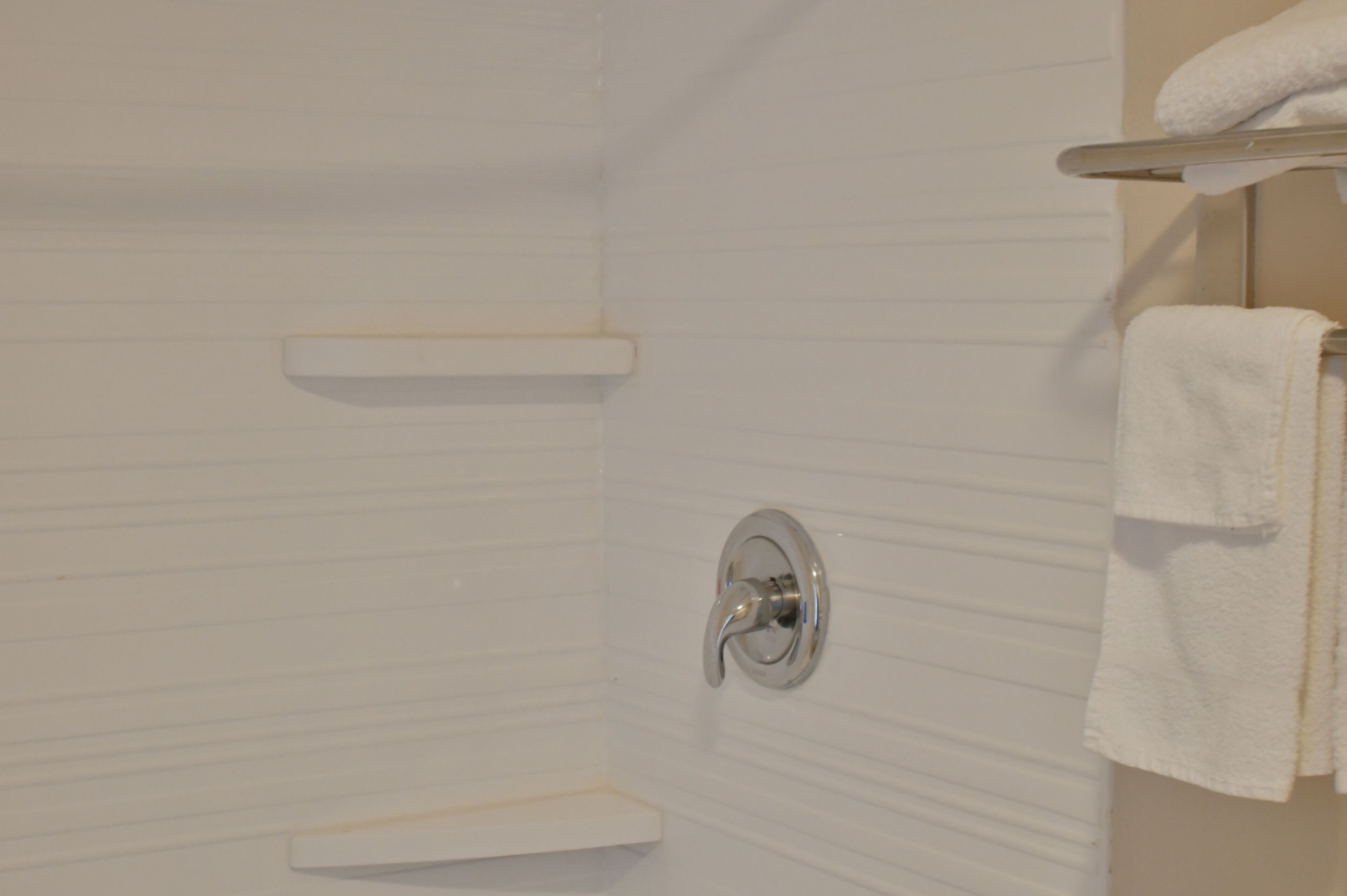 Bagno con parete piastrellata di bianco, zona doccia e porta asciugamani con un asciugamano bianco.