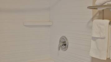 Bagno con parete piastrellata di bianco, zona doccia e porta asciugamani con un asciugamano bianco.