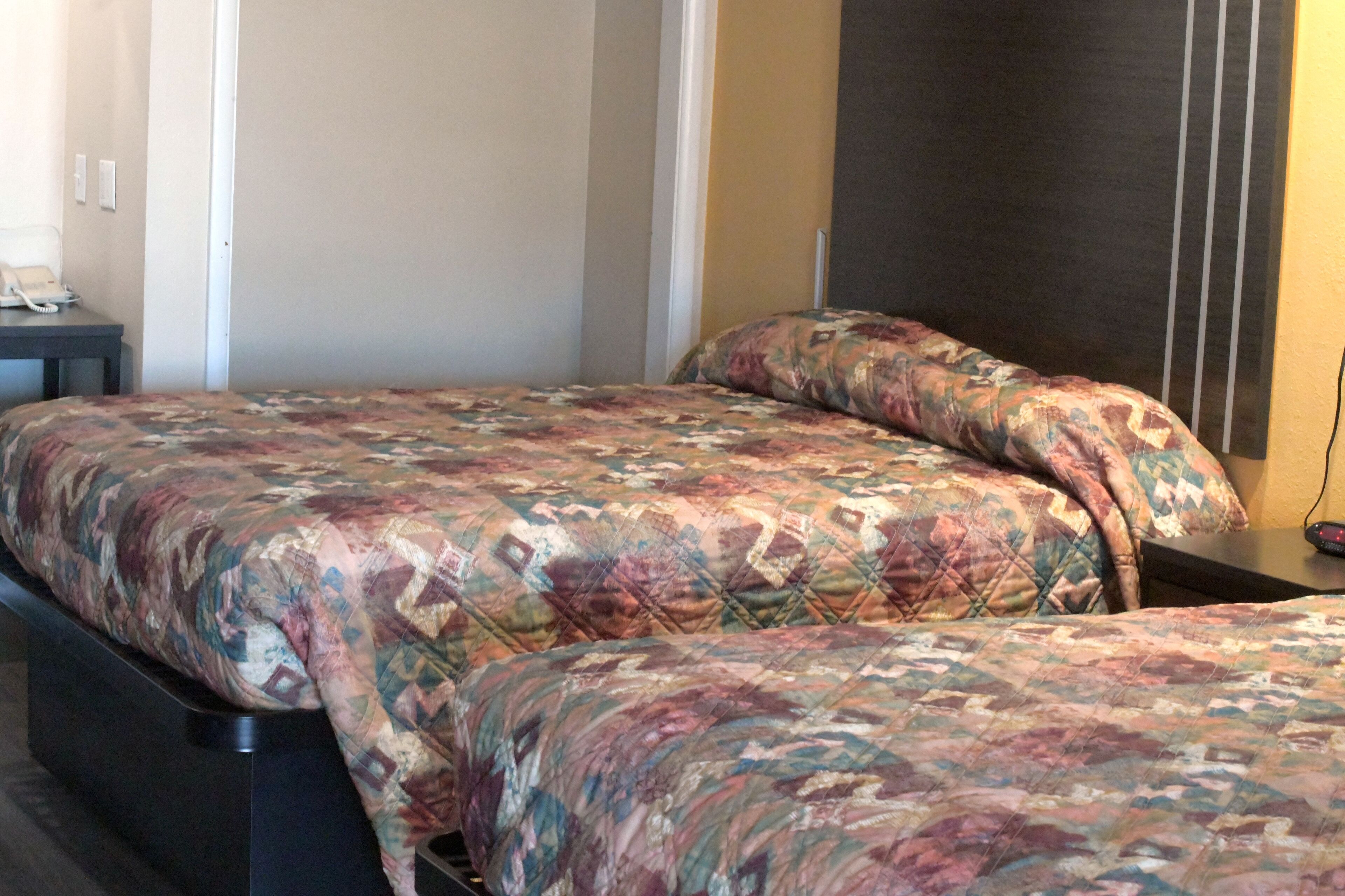 Quarto de hotel com duas camas, cada uma com colcha estampada. Há uma mesinha com telefone e uma tomada na parede.