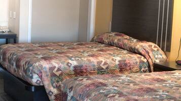 Quarto de hotel com duas camas, cada uma com colcha estampada. Há uma mesinha com telefone e uma tomada na parede.