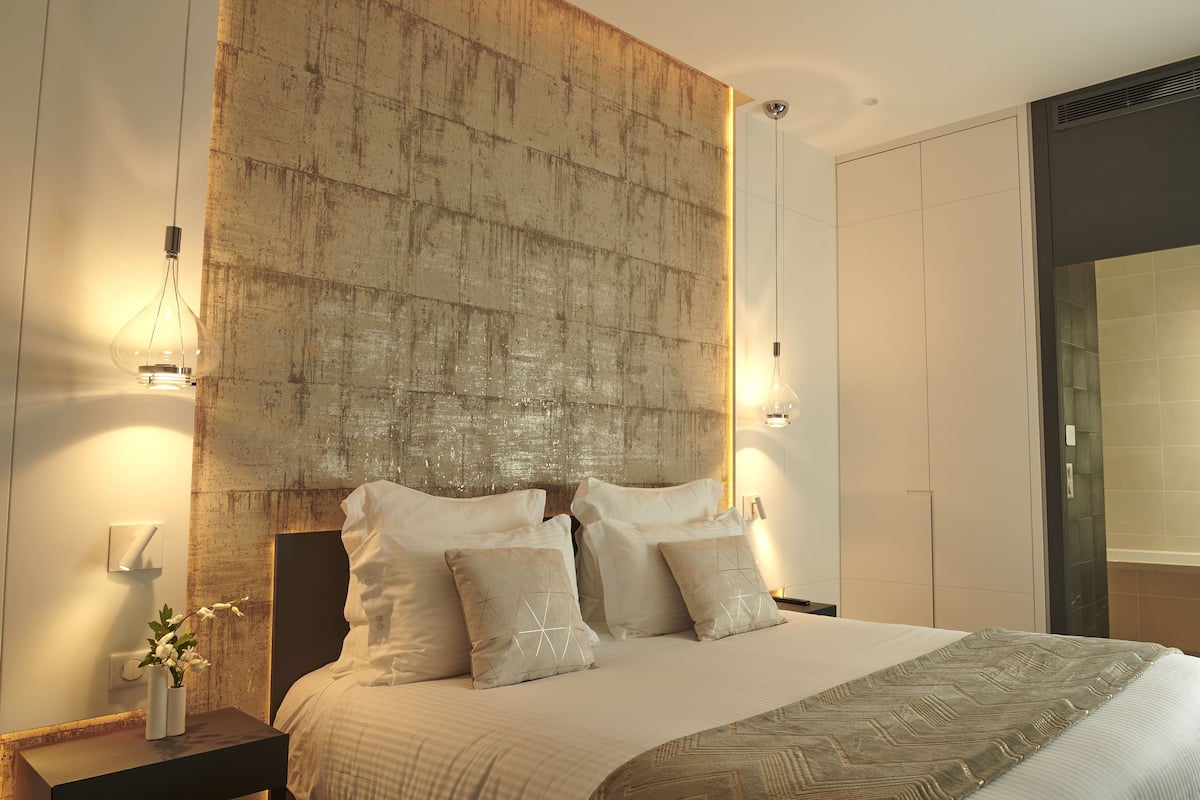 A modern bedroom with a large bed, a nightstand with a vase of flowers, and a chair by the window.