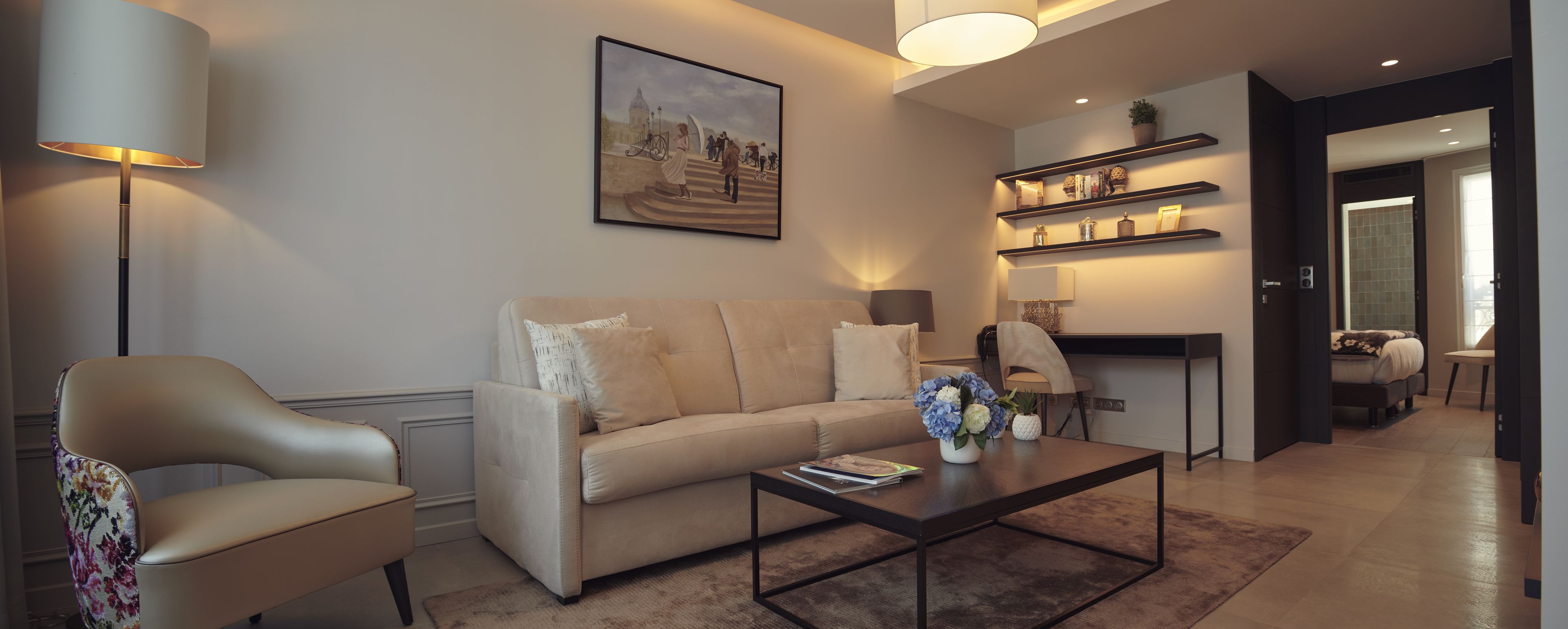 A modern living room with a sofa, armchair, coffee table, and a painting on the wall.