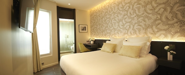 Une chambre d’hôtel avec un grand lit, une table de chevet avec une lampe, un miroir et un mur orné d’un motif décoratif.