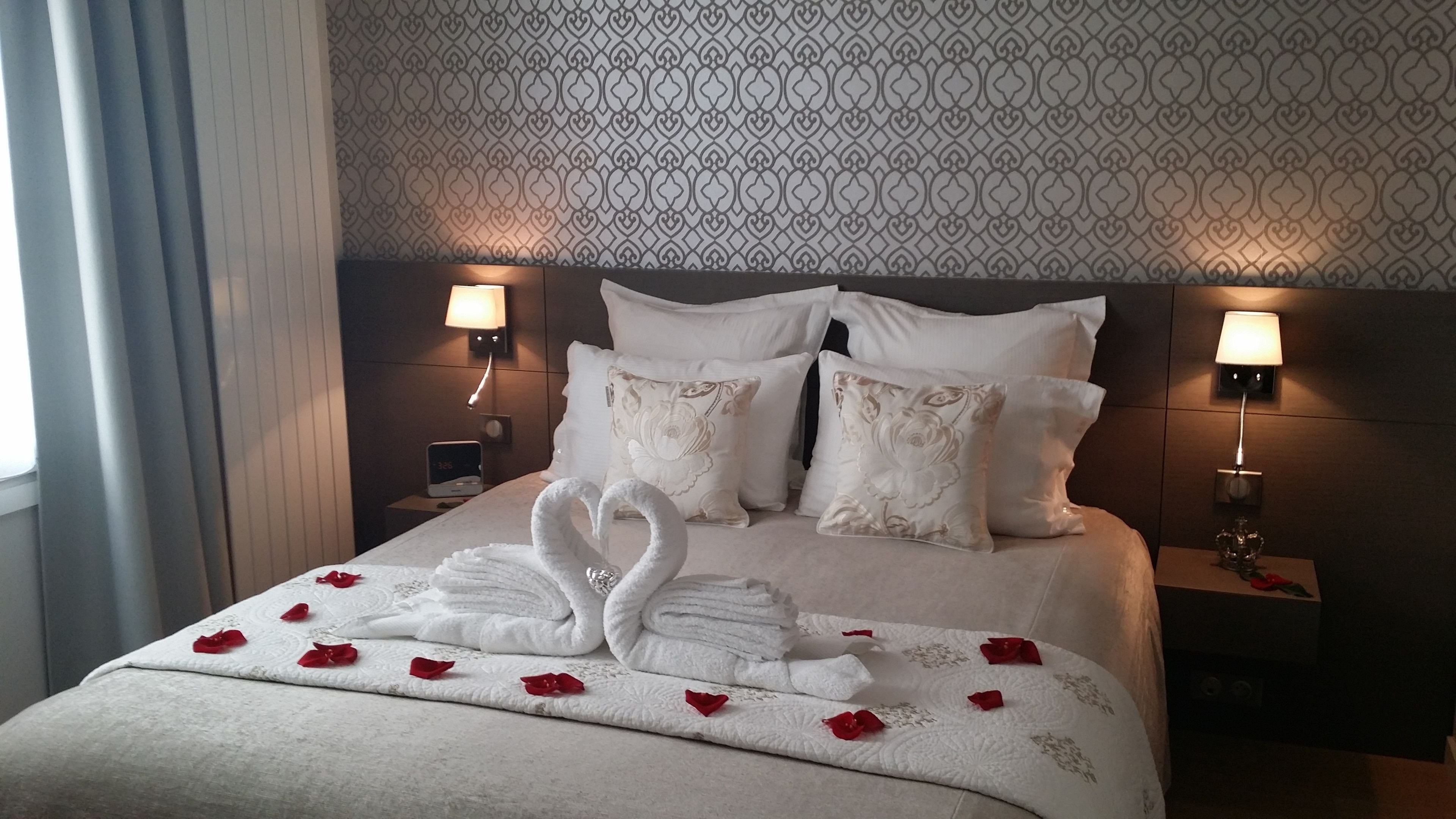 A neatly made bed with white linens, two wall-mounted lamps, and a patterned wallpaper.