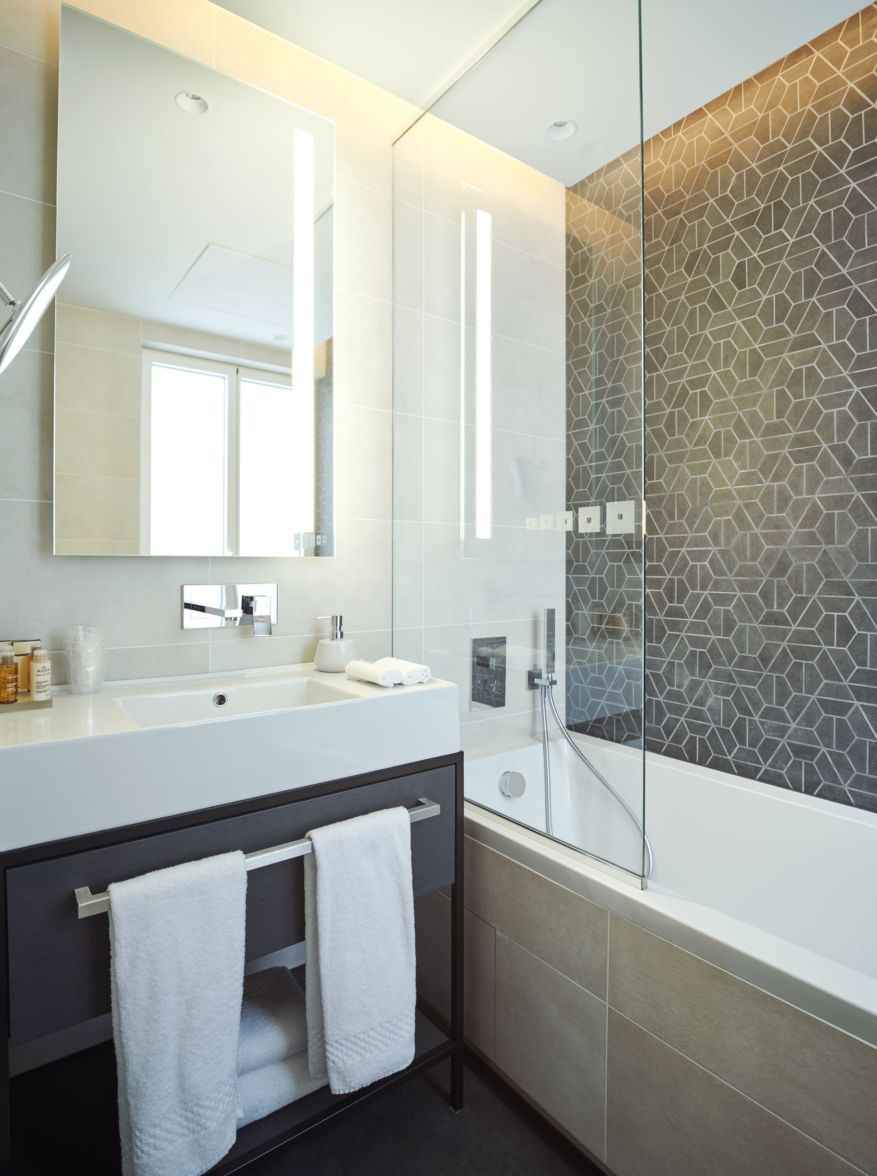 A modern bathroom with a large mirror, a white sink, a glass shower enclosure, and a dark wooden vanity.