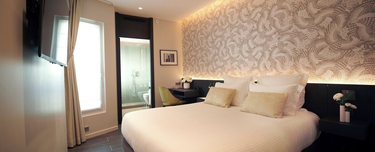 A hotel room with a large bed, a desk, a chair, a nightstand, and a wall with a decorative pattern.