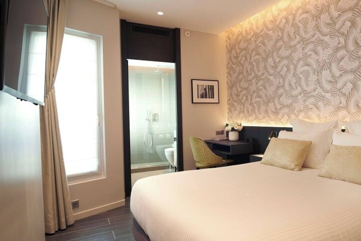 Une chambre d’hôtel avec un grand lit, un bureau, une chaise, une table de chevet et un mur orné d’un motif décoratif.
