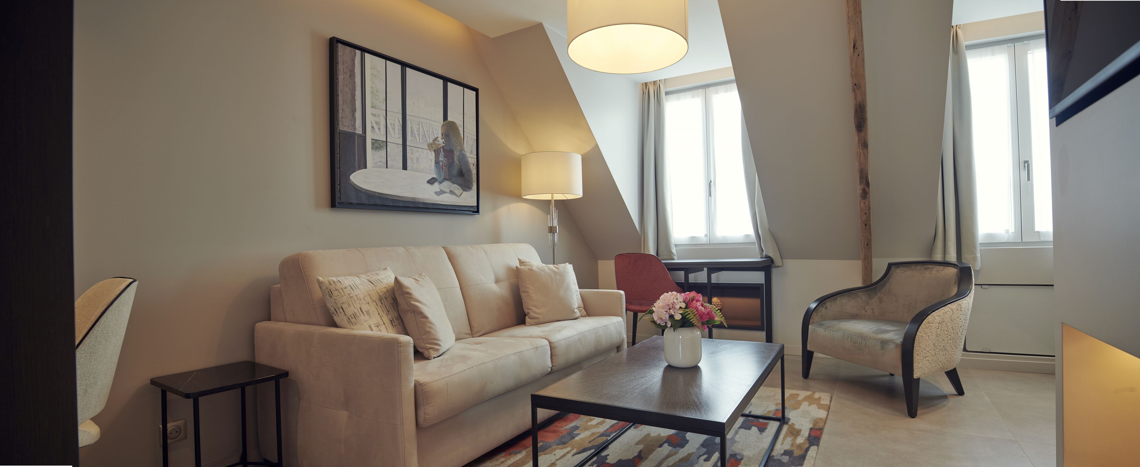 Een moderne woonkamer met een bank, een salontafel en een fauteuil. Er hangt een schilderij aan de muur en op de tafel staat een lamp.