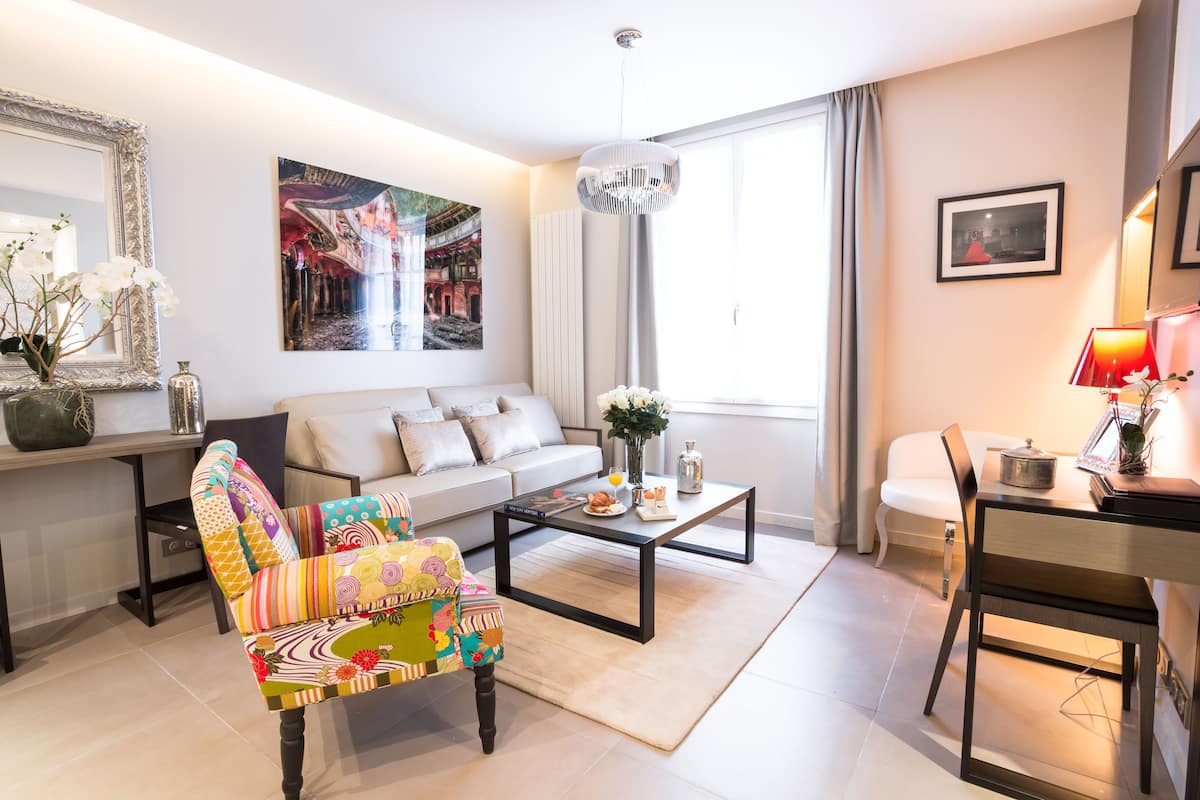 A modern living room with a sofa, colorful armchair, coffee table, and a dining area with a chair and table.