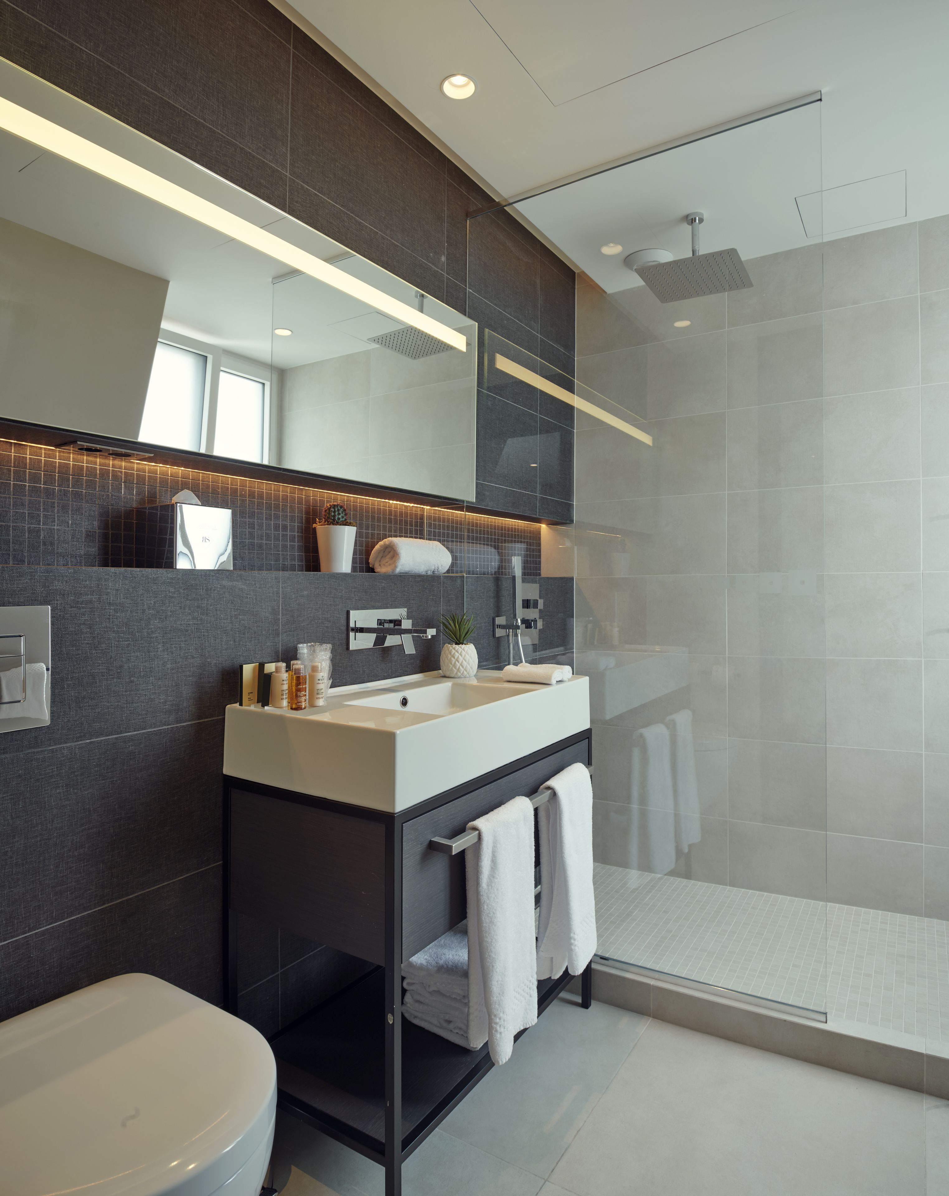 A modern bathroom with a large mirror, a shower, and a vanity with a sink.
