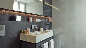 A modern bathroom with a large mirror, a shower, and a vanity with a sink.