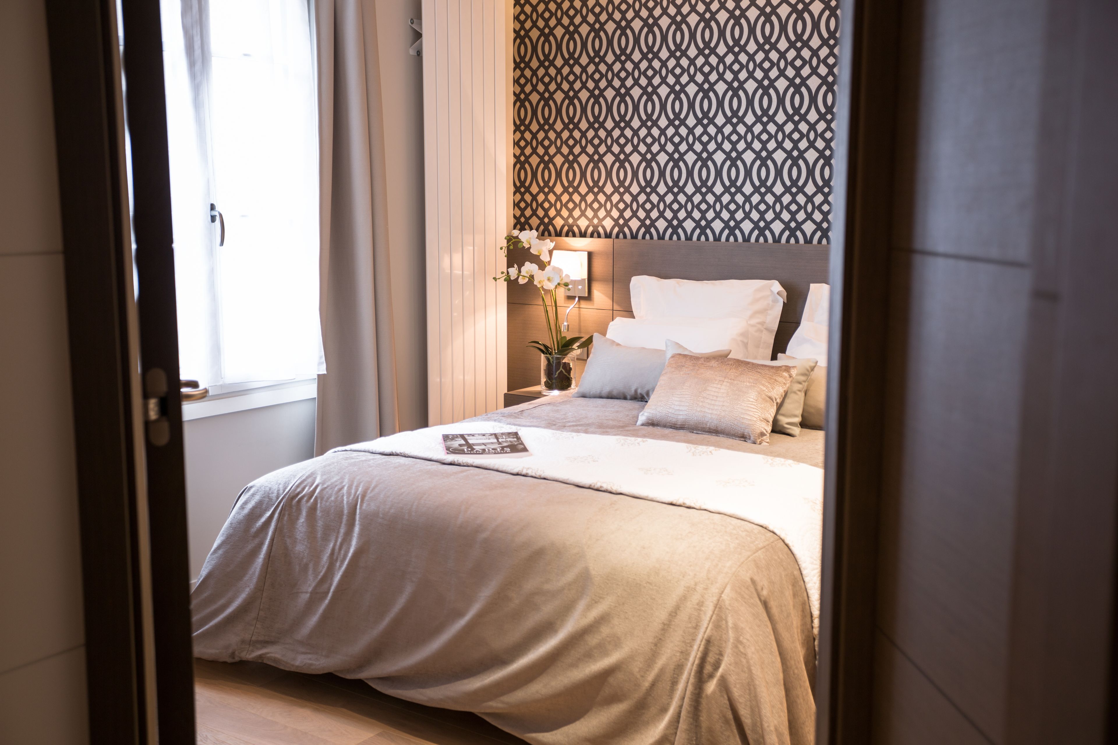 Un dormitorio con una cama grande, una mesita de noche con lámpara y un papel tapiz estampado.