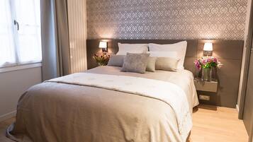 Un lit bien fait, avec une couvre-lit beige et des oreillers, deux lampes de chevet et un vase rempli de fleurs sur la table de chevet.