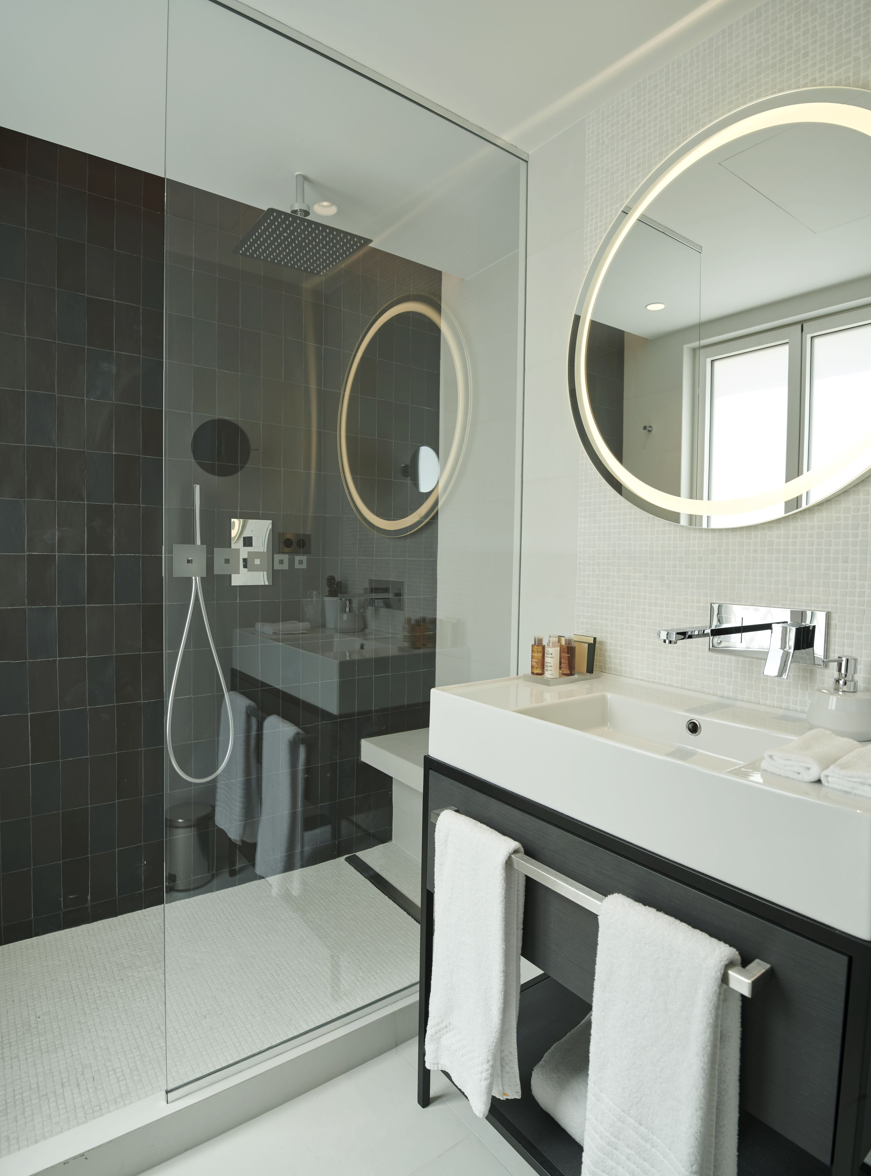 Un baño moderno con ducha de vidrio, un espejo grande y un tocador con lavabo y toallero.