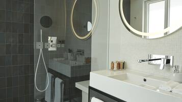 Un baño moderno con ducha de vidrio, un espejo grande y un tocador con lavabo y toallero.