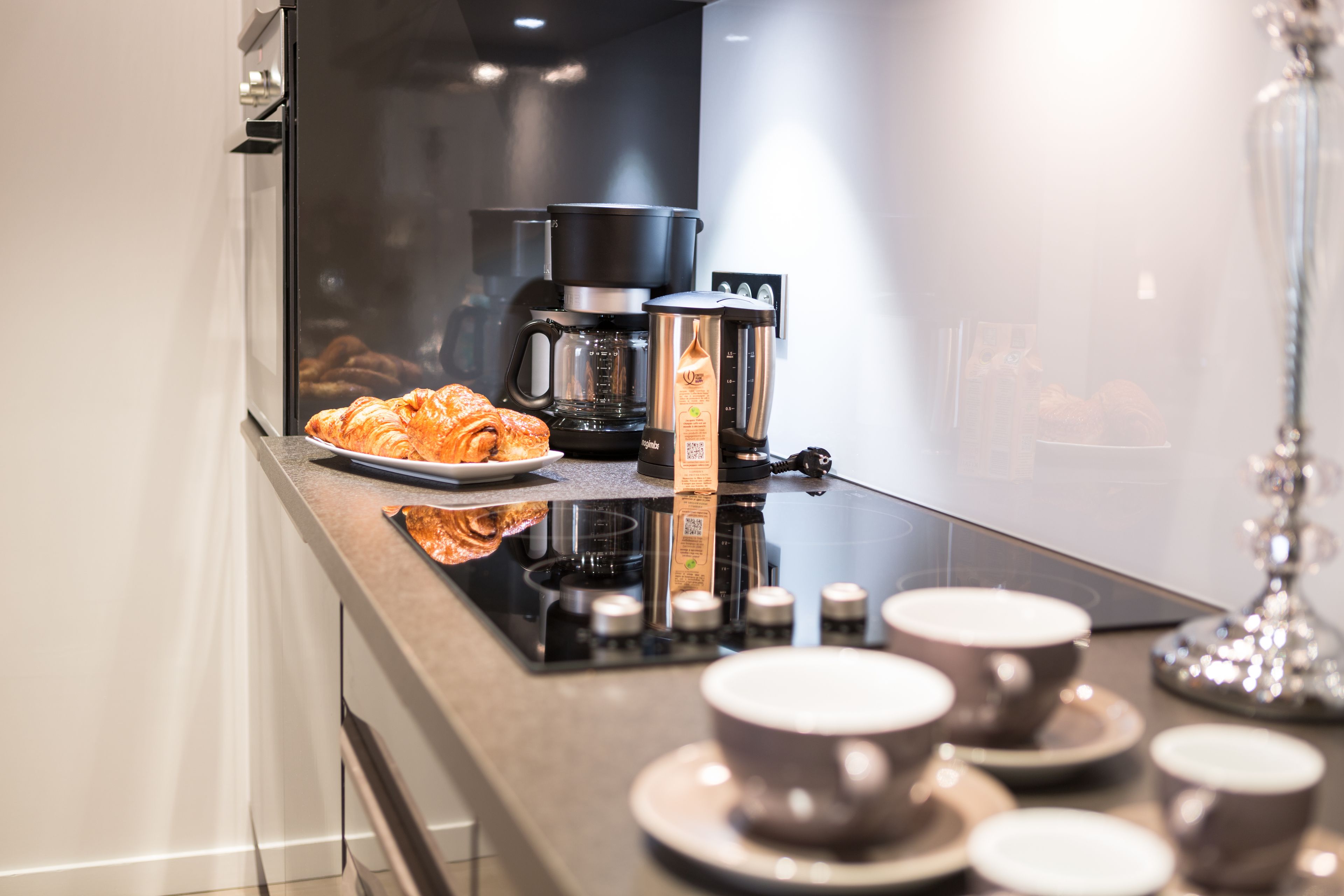 A modern kitchen with a coffee maker, a pot, and a plate of croissants.