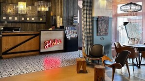 Zona de bar moderna amb un taulell de fusta, un rètol de neó que diu 'Hola' i una zona de seients amb cadires i una taula.