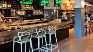 Un bar amb lletres il·luminades que diuen 'BAR', una barra plena de botelles i tres tamborets.