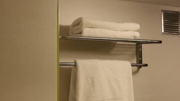 Une salle de bain avec un porte-serviettes sur lequel sont pliées deux serviettes et une autre serviette suspendue, ornée d'une broderie « NHC LATARO ».