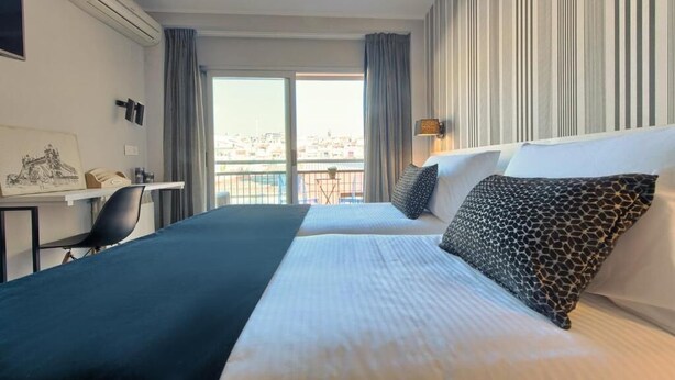Habitació d'hotel amb dos llits, un escriptori i vista a la ciutat.