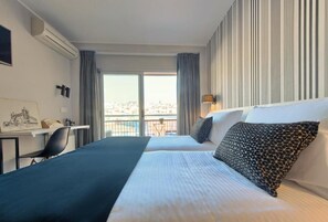 A hotel room with two beds, a desk, and a view of the city. - New Hotel Colón (Mataro)